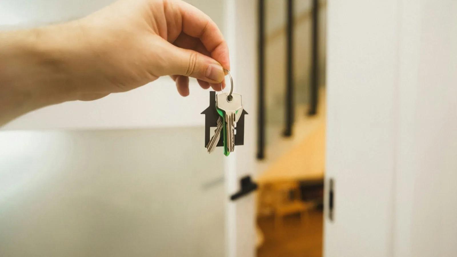 Hand håller nyckel med hus-keychain framför öppen lägenhetsdörr