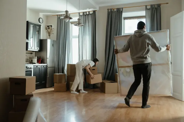 En person bär en tavla genom ett ljust kök medan en annan lyfter en kartong