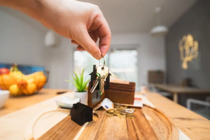 En hand håller upp en nyckelknippa över ett köksbord med en liten husfigur