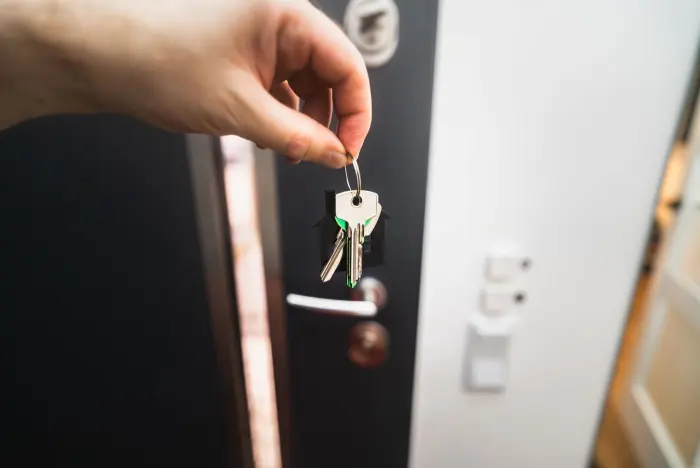 En hand håller en nyckel framför en öppen ytterdörr