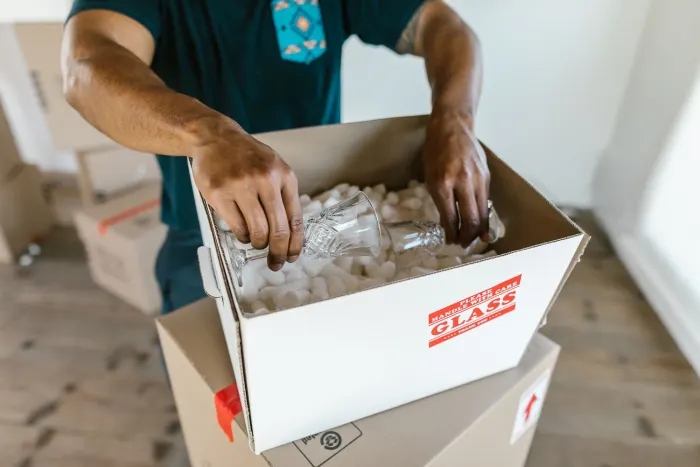 En flyttare packar glas i en kartong märkt Glass, fylld med skyddsmaterial
