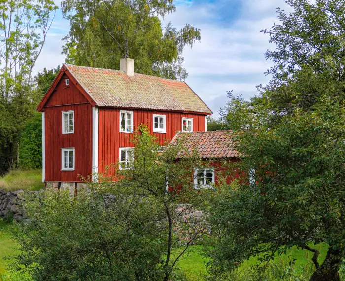 Rött trähus med vita knutar bland grönska en sommardag